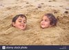 two-young-children-buried-in-sand-on-the-beach-norfolk-A2J3X4.jpg